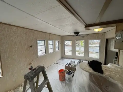 Room interior during renovation with ladder and paint supplies.